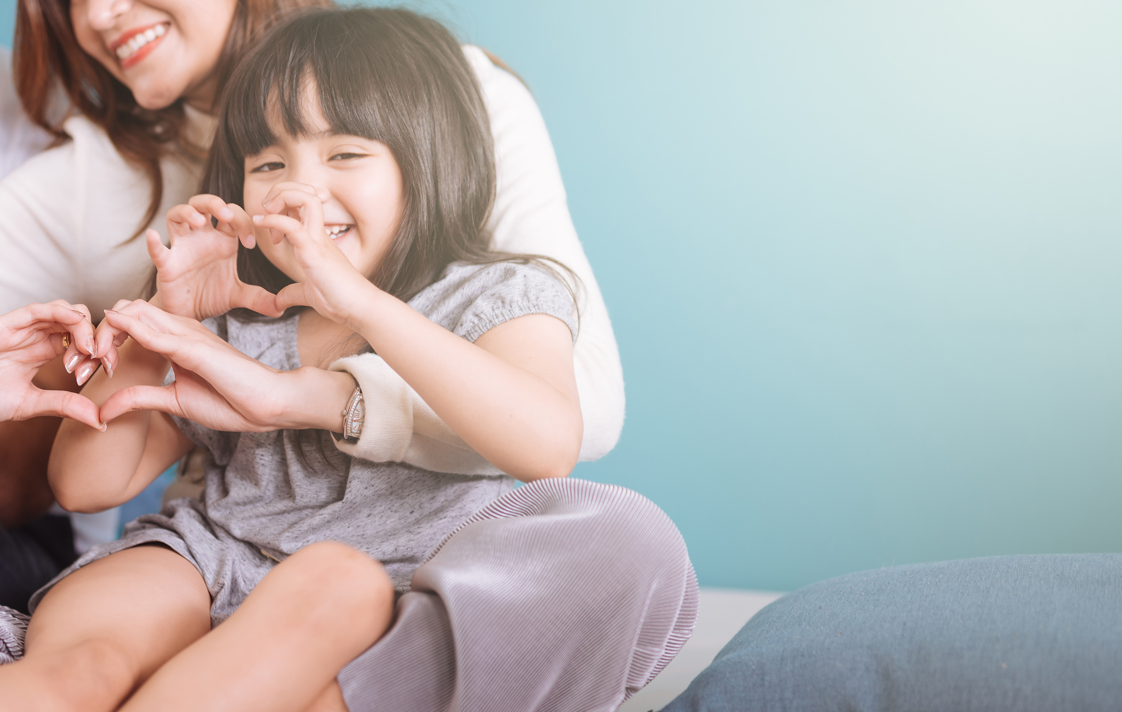 girl making heart shape sit in mom lap.